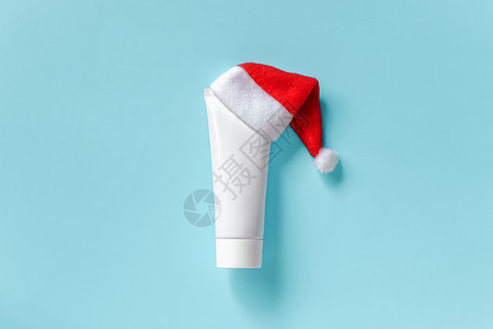 化妆品医用白色管于奶油软膏或其他产品在蓝色背景的红圣诞老人帽子概念冬季皮肤和身体护理或圣诞礼物样机顶视图复制空间模板化妆品医用白图片