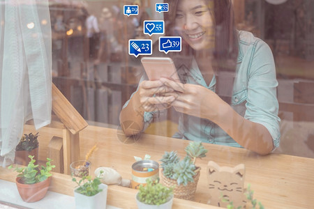 联网亚洲女商人手用智能机为社交网路媒体使用在现代咖啡店的窗口社交网络概念外包括类似爱评论人和fovotorite图标打字数的图片