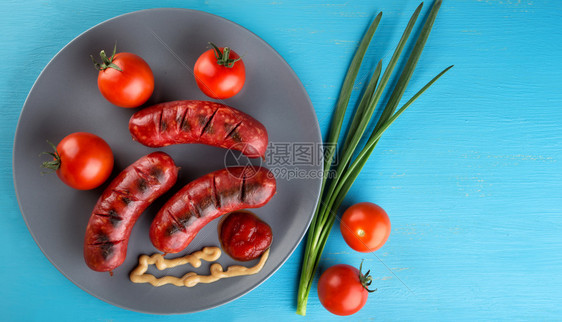 煮熟的红色香肠和番茄及料在蓝木板上传统食品美味肉的香肠与西红柿及料之概念晚餐图片