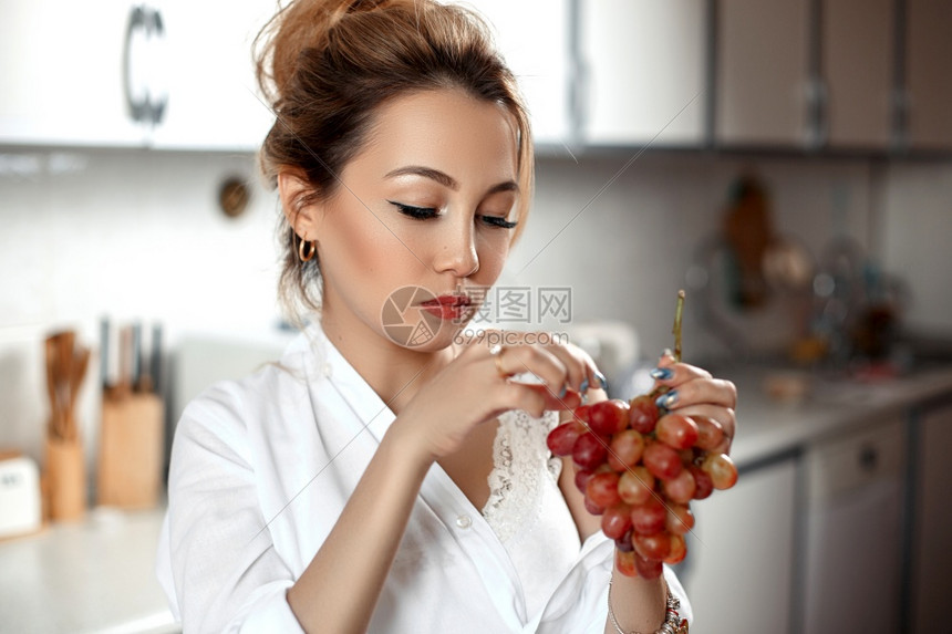 自然蕾丝成人穿着米花短裤的年轻亚洲美女在厨房有选择地集中吃葡萄的白衬衫一个小重点领域图片