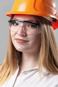 一位有魅力的年轻女子肖像金发戴橙色头盔和眼镜印在中灰背面的色玻璃上一位有吸引力的年轻女子肖像金色头发印在橙盔上的中灰色背景的美丽图片