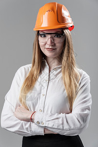 一位有魅力的年轻女子肖像金发戴橙色头盔和眼镜印在中灰背面的色玻璃上一位有吸引力的年轻女子肖像金色头发印在橙盔上的中灰色背景的建筑图片