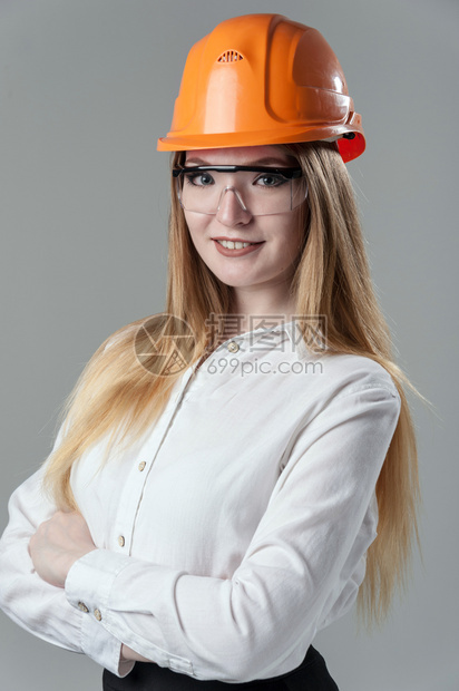 经理一位有魅力的年轻女子肖像金发戴橙色头盔和眼镜印在中灰背面的色玻璃上一位有吸引力的年轻女子肖像金色头发印在橙盔上的中灰色背景成图片