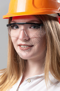 员工帽子程师一位有魅力的年轻女子肖像金发戴橙色头盔和眼镜印在中灰背面的色玻璃上一位有吸引力的年轻女子肖像金色头发印在橙盔上的中灰图片