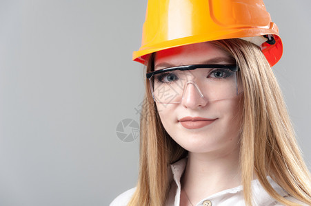 经理脸建造一位有魅力的年轻女子肖像金发戴橙色头盔和眼镜印在中灰背面的色玻璃上一位有吸引力的年轻女子肖像金色头发印在橙盔上的中灰色图片