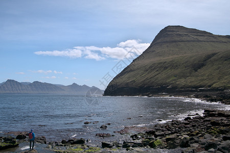 风景优美法罗群岛地貌的横向景象包括美丽的山峰和北大西洋以及无法辨别的年轻登山者站立在附近GjogvGlograflePostca图片