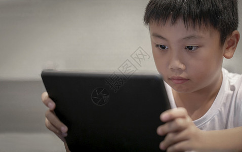 英俊的视频在家数字平板电脑上玩游戏的亚洲男孩在数字小盘或智能手机上看漫画的儿童男生图片