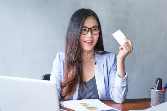 吸引人的技术淑女坐在主办公台的美丽商业妇女她们用笔记本电脑在手拿着信用卡工作时笑着微并且使用计算机室内做一个有吸引力的快乐型号图片