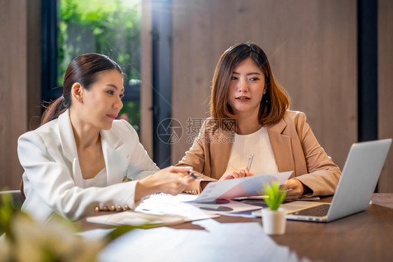 杯子在现代会议室办公或工作空间咖啡休息伙伴和同事概念中通过技术笔记本电脑与伙伴企业合作的两名亚洲女实业商人们快乐的图片