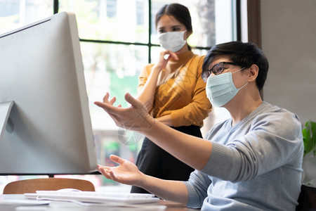 保护流行防面罩青年设计师在算机监控上工作与亚洲商人和界女一起讨论并在办公室开会时为商业工作提供咨询在办公室开会时就商业工作进行讨图片