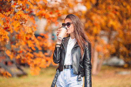 女孩头发金的美丽女人在秋天公园里在温暖的日子里在秋天的落叶下喝咖啡图片