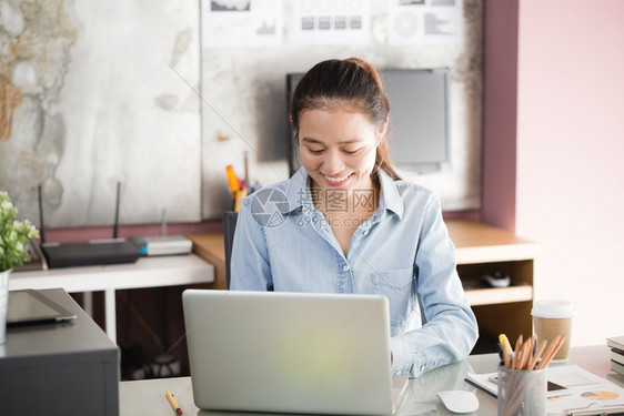 在办公室使用笔记本电脑的新一代亚洲女商人妇在努力制定移动办公室概念时微笑地坐着容成就肖像工作图片