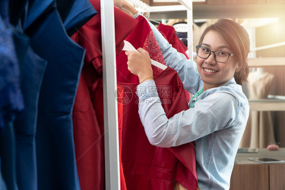 在职的造型师快乐亚洲年轻女服装设计时师正在检查能否展厅完成一件西装和服这是成功的青年创业者在时装行中的概念办公室图片