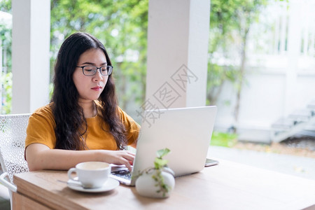 年轻的在咖啡店用笔记本电脑咖啡杯和智能手机如背景通信概念等工作的女散校对Portnoyunorg桌子在线的图片