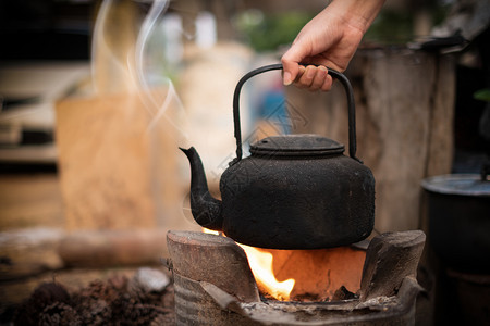 抽烟野餐厨师紧握着煮水的手在火上装满旧茶壶背景模糊的木炭炉灶图片