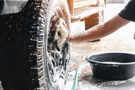 车辆洗工作人员正在使用肥皂和水浸湿的海绵清洗汽车轮子蜡泡沫图片
