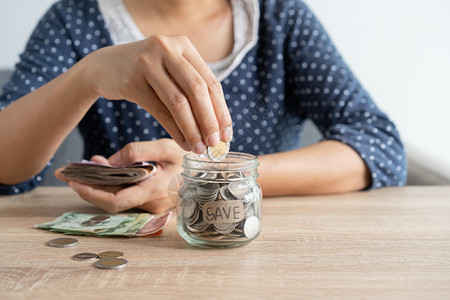 会计桩生长亚洲女手把一枚硬币放在玻璃瓶里一块硬币放在家里桌上的投资企业和退休融为未来的概念节省钱财注图片