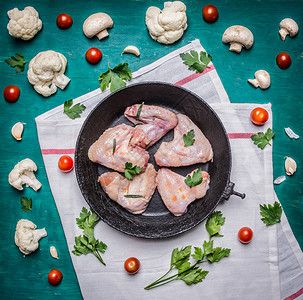 鲜生鸡翅在古老的铸铁椰菜花番茄蘑菇和草药中在一个白色餐巾纸上以锈木背景为顶尖视野翅膀生的厨师图片