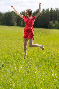 乐趣年轻的穿红裙子年轻女孩在阳光明媚的一天在田里跳跃成人图片