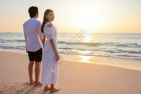 年轻的亚洲快乐情侣在海滩上握着手与一个女人面对相机鼓浪漫旅行蜜月渡暑假亚裔女和男手拥抱户外的日落背景晴天一种喜悦图片