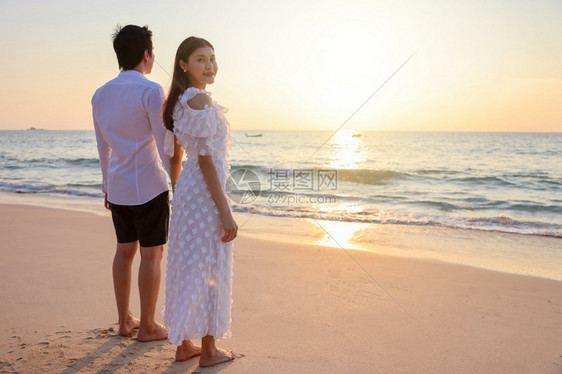 年轻的亚洲快乐情侣在海滩上握着手与一个女人面对相机鼓浪漫旅行蜜月渡暑假亚裔女和男手拥抱户外的日落背景晴天一种喜悦图片