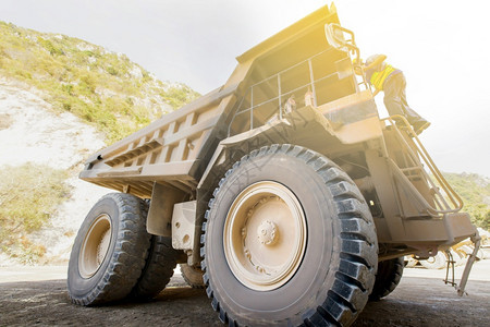 漏洞水泥男司机在山区附近一个露天坑的大型采矿倾卸卡车楼梯上走过一辆大型采矿倾卸车重的图片