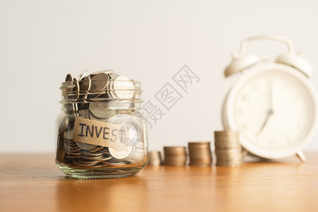 收入预算一个玻璃瓶中的硬币一堆和棕色木桌上的白回转闹钟投资退休金融和储蓄业务以备未来概念的构想时间图片