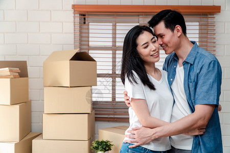 买下新婚夫妇开始生活的概念在购买新家后搬来的路上用纸板盒拥抱男友时使用纸板盒拥抱着男朋友的年轻亚洲快乐情侣微笑包装房主乐趣图片