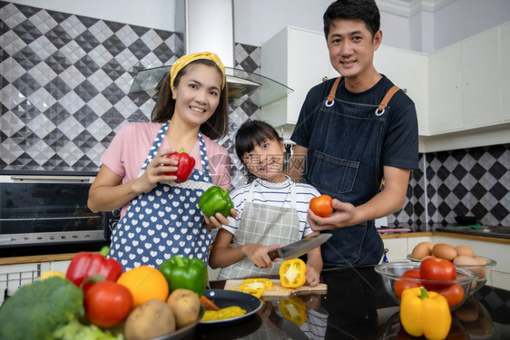 快乐的家庭有爸妈和她们的女儿在厨房一起烹饪笑声橙食物微图片