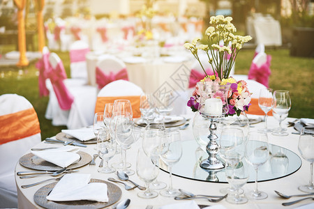 装满水酒和餐具的空杯子装花饰品和白布条带粉色礼巾的桌椅并配有花瓶场地勺子图片