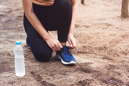 女人在森林里慢跑时绑起鞋带着饮用水瓶回到森林边上妇女们用自来水瓶把人和生活方式概念捆绑在一起保健和福利主题公园和户外主题慢跑者腿图片