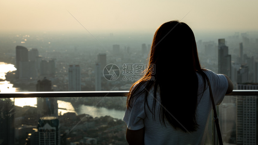 生活阳光女孩站在楼顶的屋上看着城市满是尘土和空气污染还有日出背景晚上泰国曼谷时分在清晨后夜天空图片