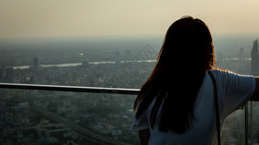 户外常设女孩站在楼顶的屋上看着城市满是尘土和空气污染还有日出背景晚上泰国曼谷时分在清晨后夜独自的图片