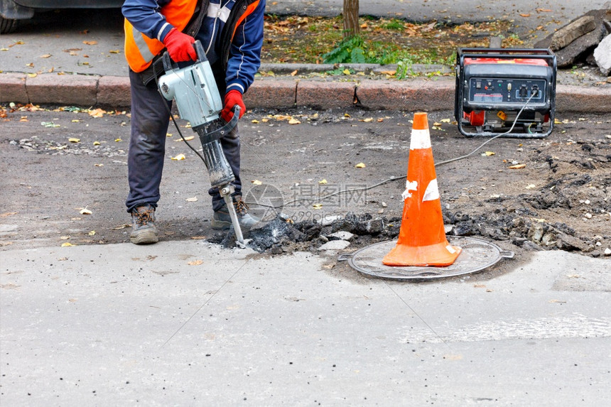 人行道手一名身穿反光衣服的公路工人在修理围栏路段时用电动大锤打碎旧沥青A工人使用电动大锤来松开旧沥青钻头图片