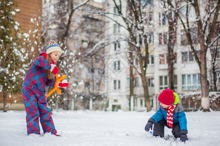 快活女孩雪地乐的兄弟姐妹在冬季散步时打雪球在公园里做雪球冬季户外游戏快乐的兄弟姐妹在冬季散步时玩雪球在公园里做雪球图片