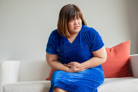 在客厅沙发上坐的超大亚洲妇女她不开心和快乐手抱腹部疼痛的膀胱时间抽搐胃炎和保健概念经期人们便秘图片