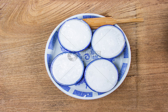 传统一种的泰国椰子牛奶碗是用面粉椰子奶和糖制成的泰式甜点把小型陶瓷杯放在木制地板上图片