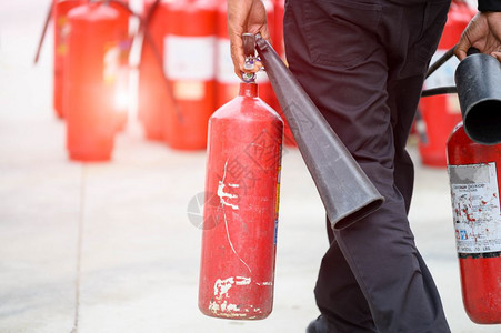 战术工具热的消防员下身紧闭准备进行消防演习方法是持有手提式灭火器和水管安全保险防护和消战士概念许多红色干化学品罐背景图片