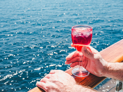 奢华船人们在蓝海浪背景下游轮露天甲板上盛着一杯美丽的粉红葡萄酒时装男子侧观特近休闲和旅行概念暇和旅游概念持有美丽粉红葡萄酒的人图片