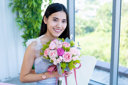 情人节的概念笑亚裔年轻女坐在餐桌上吃着食物在餐厅背景中拿着一束玫瑰花朵的欢乐快仪式婚礼年轻的图片