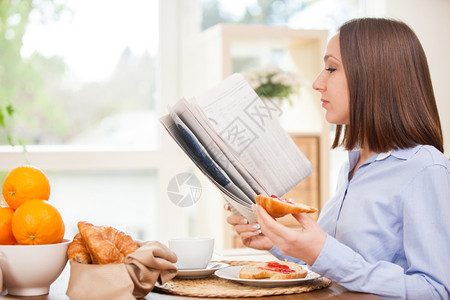 闲暇经济照片黑发女商人在家吃早餐时看报纸的照片注肖像图片