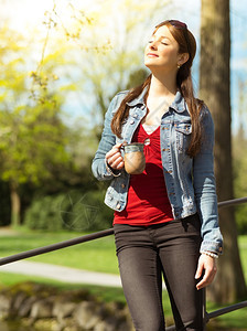 常设一位美丽的年轻女子在户外享受阳光的温暖时喝着咖啡或茶叶她的相片吸引人年轻图片