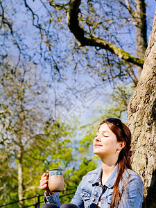 成人马克杯夏天一位美丽的年轻女子坐在户外享受阳光温暖时喝咖啡或茶的照片她脸被遮着图片