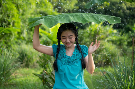 在绿花园背景下雨时一位年轻亚洲女身着香蕉叶的黑头发肖像抓住漂亮的愉快图片