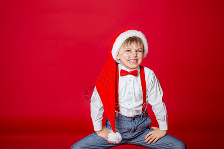 跌倒可爱的情绪圣诞快乐可爱开朗狡猾的小男孩戴着红色背景的圣诞老人帽子一个快乐的童年有梦想和礼物图片