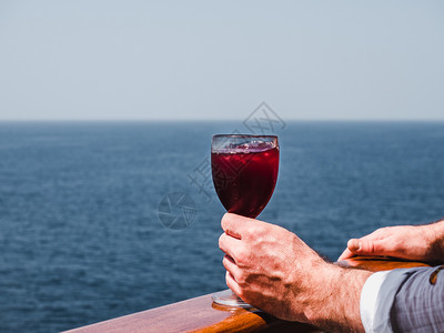 手红色的日出在蓝海浪背景下游轮露天甲板上盛着一杯美丽的粉红葡萄酒时装男子侧观特近休闲和旅行概念暇和旅游概念持有美丽粉红葡萄酒的人图片