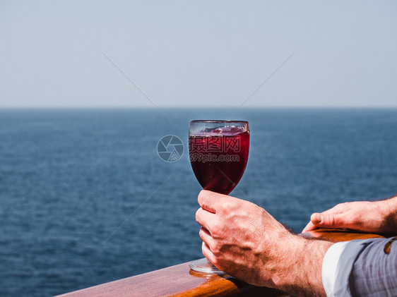 手红色的日出在蓝海浪背景下游轮露天甲板上盛着一杯美丽的粉红葡萄酒时装男子侧观特近休闲和旅行概念暇和旅游概念持有美丽粉红葡萄酒的人图片