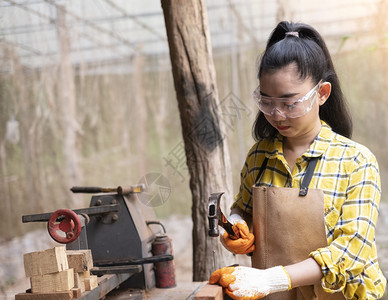 女专业的常设妇女站立建筑工身着经检查的衬衫在建筑工地作在木板上钉图片
