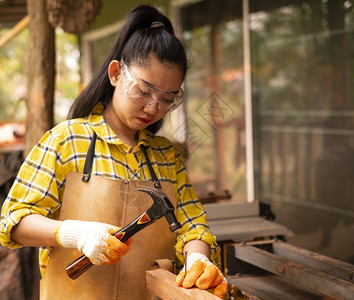 肖像工具锤子妇女站立建筑工身着经检查的衬衫在建筑工地作在木板上钉图片