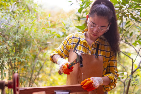 建造指甲成人妇女站立建筑工身着经检查的衬衫在建筑工地作在木板上钉图片